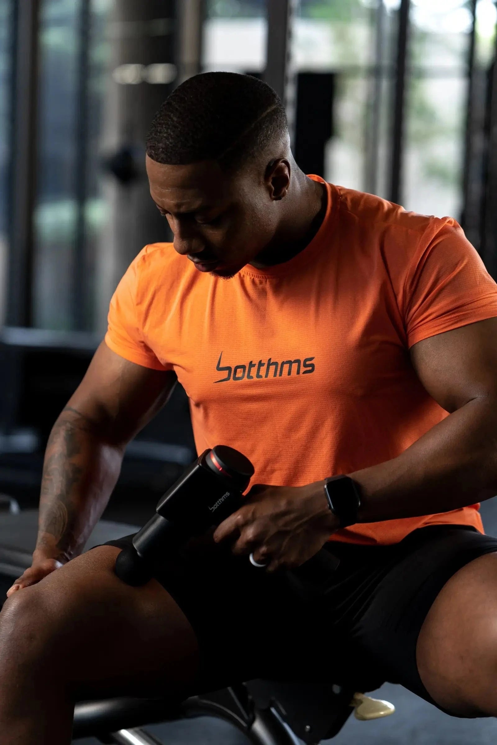 athlete applying botthms massage gun on his right leg muscle
